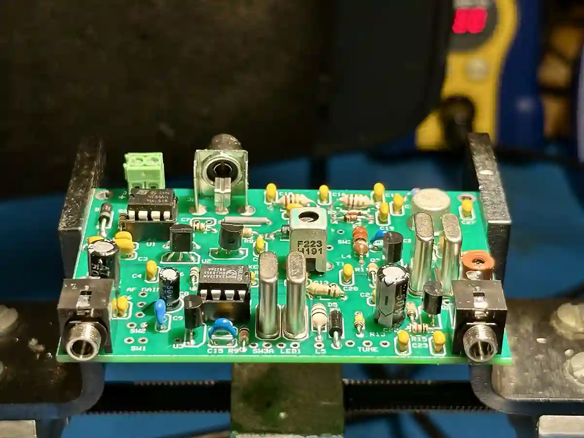 Partially built 40-meter Woodpecker CW transceiver kit. The green circuit board is mounted in a PCB vise, with most components soldered on, including capacitors, resistors, and ICs.